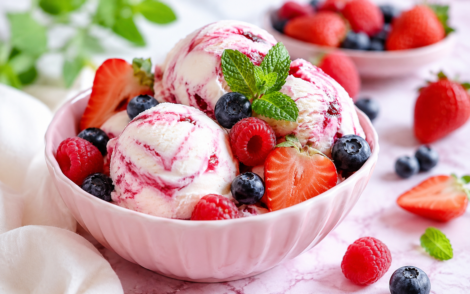 Berry swirl ice cream scoops with strawberries, raspberries, blueberries, and fresh mint in a pink bowl