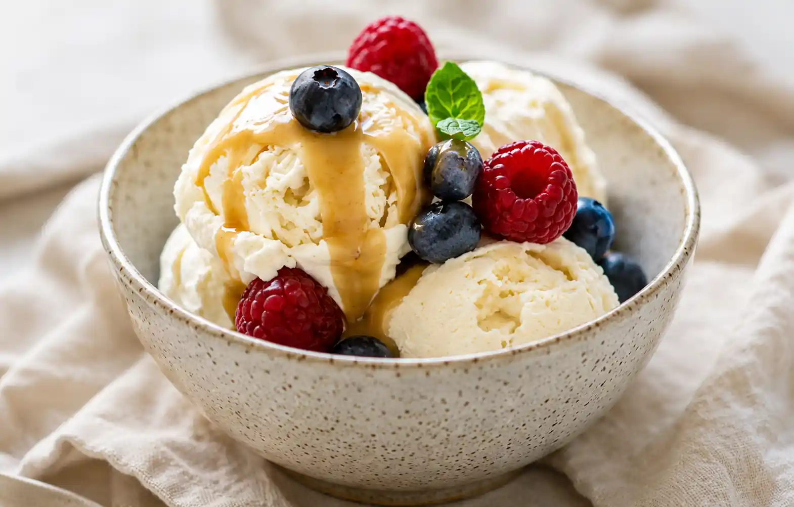 Creamy vanilla ice cream with raspberries, blueberries, fresh mint, and caramel sauce in a ceramic bowl